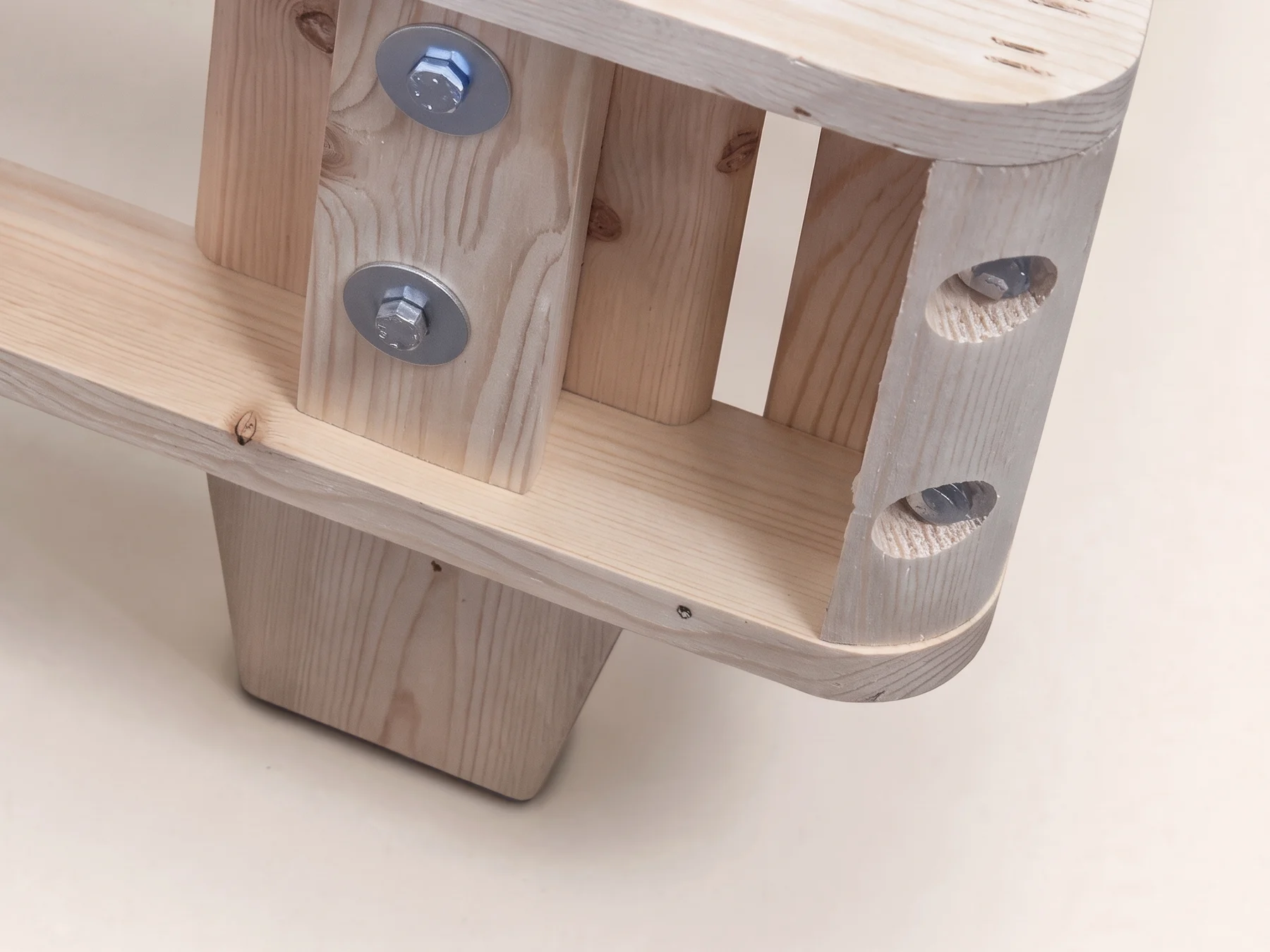 A tapered solid spruce leg bolted under the corner of the heavy-duty foundation, with the two-bolt corner joint above it