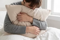 Woman hugging a natural shredded latex pillow on organic cotton bedding