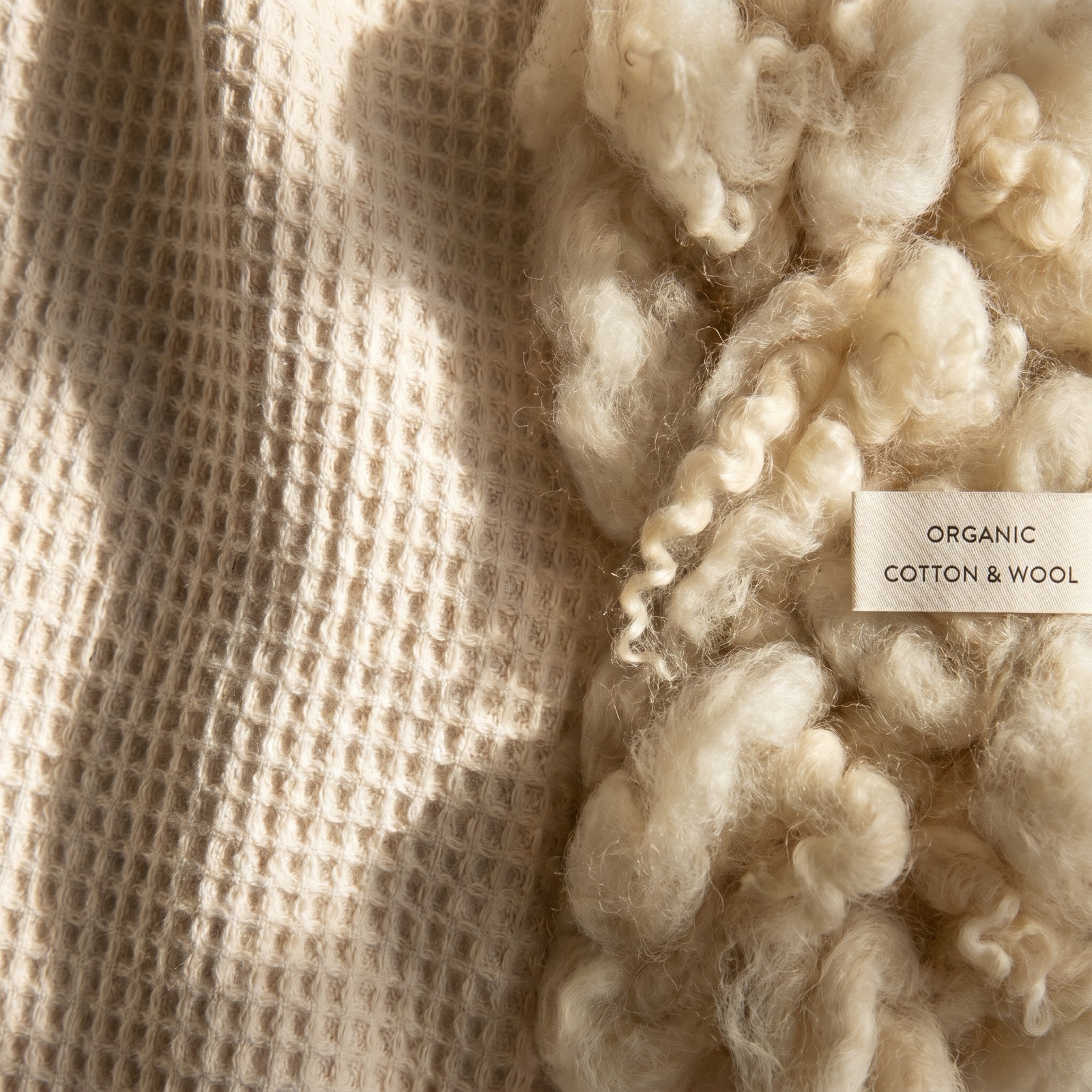 Macro close-up of organic cotton fabric weave alongside natural cream-colored wool fibers